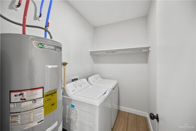 Washroom featuring wood finished floors, electric water heater, washer and dryer, baseboards, and laundry area