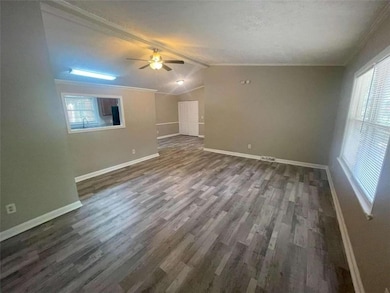 Unfurnished living room featuring a ceiling fan, vaulted ceiling, healthy amount of natural light, dark wood-style floors, and ornamental molding