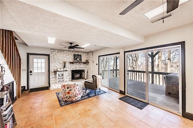 Living room featuring a textured ceiling, a skylight, visible vents, a ceiling fan, and a stone fireplace