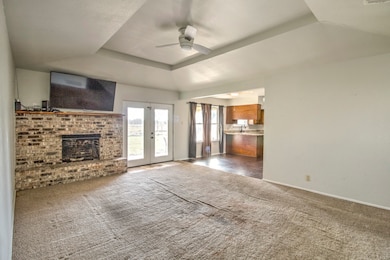 Unfurnished living room with a raised ceiling, dark colored carpet, a fireplace, french doors, and ceiling fan