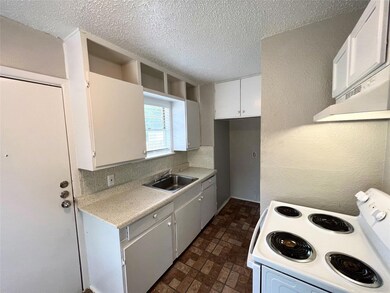Kitchen featuring dark tile floors, range, white cabinets, sink, and a textured ceiling