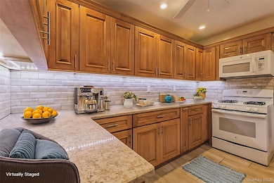 Kitchen featuring white appliances, brown cabinetry, decorative backsplash, light stone countertops, and recessed lighting