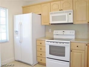 Kitchen with light brown cabinetry and white appliances