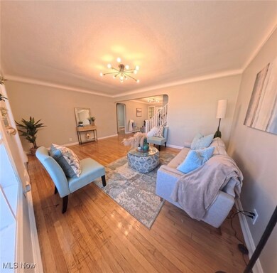 Living area with arched walkways, wood-type flooring, stairs, a textured ceiling, and a chandelier