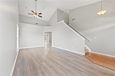 Unfurnished living room featuring high vaulted ceiling, light wood finished floors, ceiling fan, and stairway