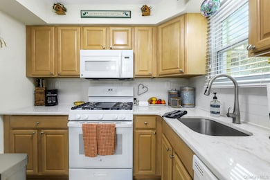 Kitchen with white appliances, decorative backsplash, light stone countertops, and brown cabinetry, window