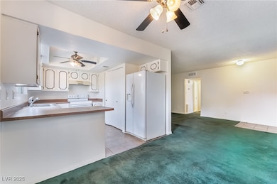 Kitchen featuring light colored carpet, white appliances, light tile patterned flooring, a ceiling fan, and a textured ceiling