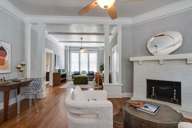 Living room with decorative columns, ceiling fan, wood finished floors, ornamental molding, and a brick fireplace