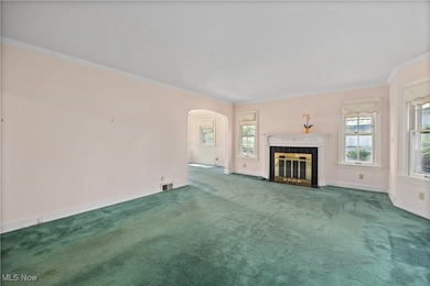 Unfurnished living room featuring arched walkways, ornamental molding, carpet flooring, and a fireplace