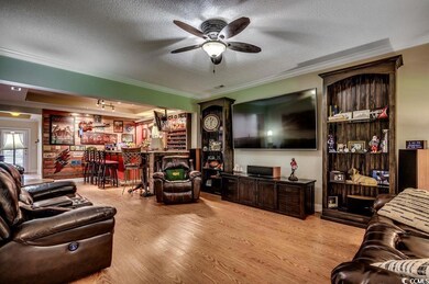 Living room with a bar, crown molding, wood finished floors, ceiling fan, and a textured ceiling