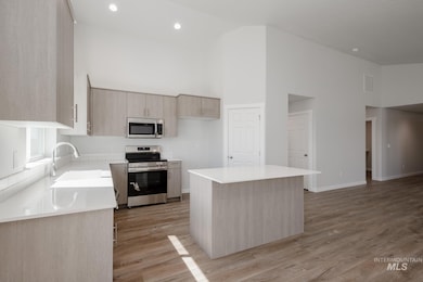Kitchen featuring high vaulted ceiling, stainless steel appliances, a kitchen island, light brown cabinetry, and light wood-style floors