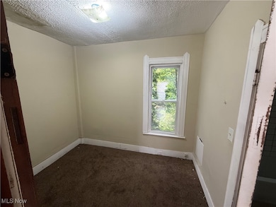Empty room featuring dark carpet and a textured ceiling