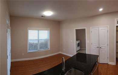 Kitchen with washer / clothes dryer, dark stone countertops, sink, stainless steel dishwasher, and dark tile flooring