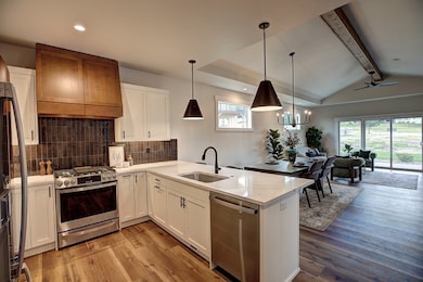 Kitchen featuring appliances with stainless steel finishes, tasteful backsplash, a peninsula, light wood-type flooring, and custom range hood