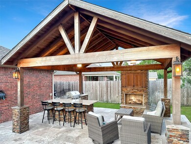 Gorgeous covered outdoor kitchen with gas-log fireplace, grill, sink, side burner, fridge, and built-in TV is a perfect place to relax year round.