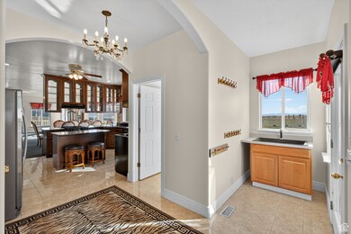 Front entry way through mud room into kitchen, a chandelier, freestanding refrigerator, see through cabinets, and hanging light fixtures.