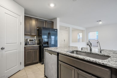Kitchen with dark brown cabinetry, stainless steel dishwasher, light stone counters, light tile patterned floors, and black fridge