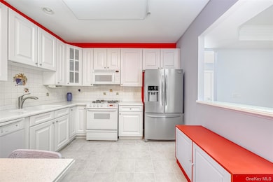 Kitchen featuring white appliances, backsplash, glass insert cabinets, white cabinets, and light tile patterned flooring