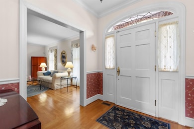 Foyer entrance featuring ornamental molding, light wood-style flooring, plenty of natural light, wainscoting, and wallpapered walls