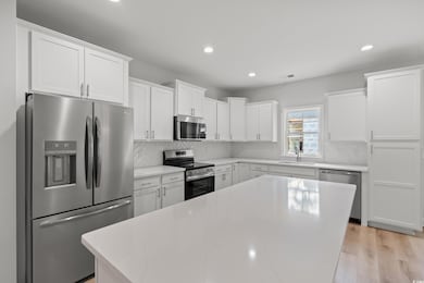 Kitchen with stainless steel appliances, white cabinets, backsplash, recessed lighting, and light wood-style flooring