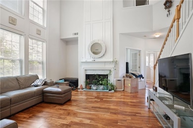 Living room featuring a towering ceiling, light wood finished floors, a fireplace with raised hearth, and stairs