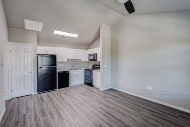 Kitchen with light countertops, black appliances, white cabinets, vaulted ceiling, and light wood finished floors