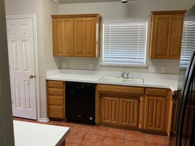 Kitchen featuring light countertops, black appliances, light tile patterned flooring, and brown cabinets