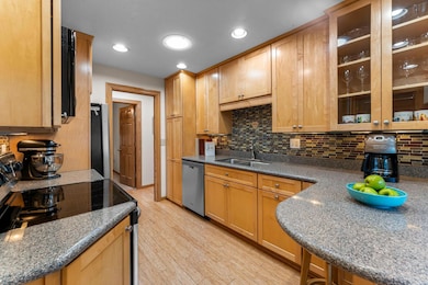 The kitchen features hardwood flooring that extends throughout the main level and is beautifully complemented by ample wood cabinetry, granite countertops, stainless steel appliances, under-cabinet lighting, and a stylish tile backsplash.