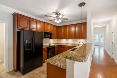 Kitchen featuring brown cabinets, black appliances, a peninsula, hanging light fixtures, and ceiling fan