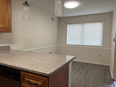 Kitchen featuring brown cabinets, dark wood-style flooring, light stone countertops, stainless steel dishwasher, and a peninsula