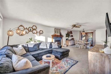 Carpeted living area with natural light, a glass covered fireplace, and a ceiling fan