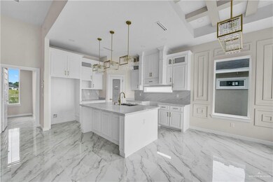 Kitchen featuring a sink, baseboards, a chandelier, coffered ceiling, and white cabinetry