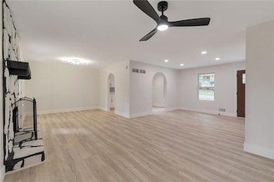 Unfurnished living room featuring arched walkways, a ceiling fan, recessed lighting, and light wood finished floors