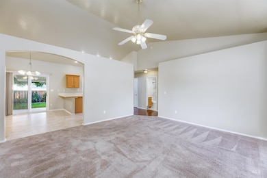 Unfurnished living room featuring light colored carpet, a chandelier, a ceiling fan, high vaulted ceiling, and arched walkways