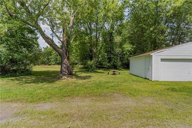 View of grassy yard featuring view of wooded area, an outbuilding, and a garage