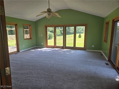Unfurnished room featuring vaulted ceiling, healthy amount of natural light, carpet, and a ceiling fan