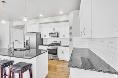 Kitchen with appliances with stainless steel finishes, a breakfast bar area, white cabinetry, pendant lighting, and granite countertops