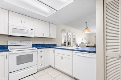 Kitchen featuring white appliances, white cabinetry, a textured ceiling, light tile patterned flooring, and dark countertops