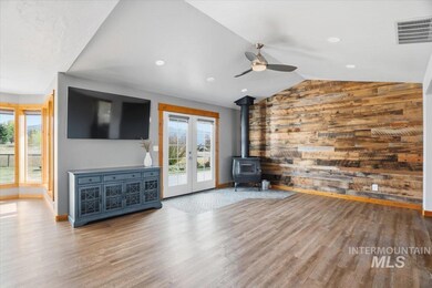 Unfurnished living room featuring a wood stove, wood walls, wood finished floors, lofted ceiling, and a ceiling fan