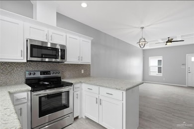 Kitchen featuring light wood-style floors, tasteful backsplash, a peninsula, white cabinetry, and appliances with stainless steel finishes