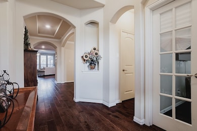 Corridor with arched walkways, dark wood finished floors, and ornamental molding