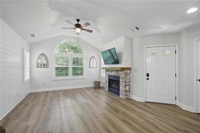 Unfurnished living room featuring wood finished floors, a ceiling fan, a fireplace, lofted ceiling, and baseboards