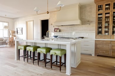 Kitchen with white cabinets, decorative backsplash, premium range hood, crown molding, and a kitchen bar
