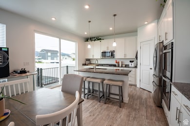 Kitchen featuring dark stone countertops, light wood finished floors, recessed lighting, decorative light fixtures, and white cabinetry