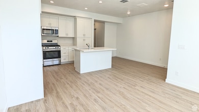 Kitchen with recessed lighting, appliances with stainless steel finishes, light wood-style flooring, an island with sink, and white cabinets (pictures are of a previous home built)