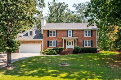 Colonial inspired home with a front yard, concrete driveway, a chimney, and brick siding
