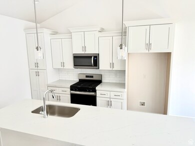 Kitchen featuring stainless steel appliances, vaulted ceiling, backsplash, white cabinetry, and decorative light fixtures