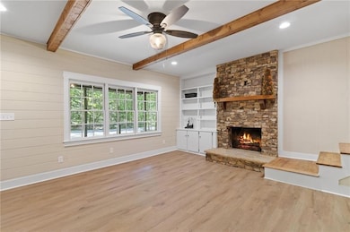 living room with wooden walls, beam ceiling, light wood-type flooring, a fireplace, and a ceiling fan
