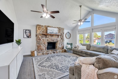 Carpeted living area with beam ceiling, stone fireplace, ceiling fans, and high vaulted ceiling
