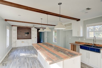 Kitchen with healthy amount of natural light, white cabinets, light wood-style floors, and beam ceiling
